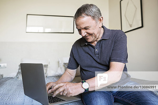 Happy senior man using laptop in bedroom