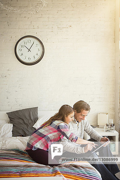 Tochter und Vater benutzen Tablet-Computer  während sie auf dem Bett sitzen