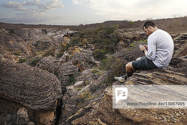 Mann sitzt auf Felsen und benutzt Smartphone