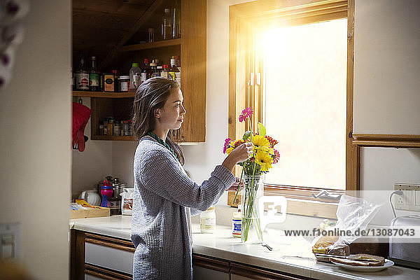 Seitenansicht einer Frau  die Blumen in einer Vase auf dem Küchentisch arrangiert