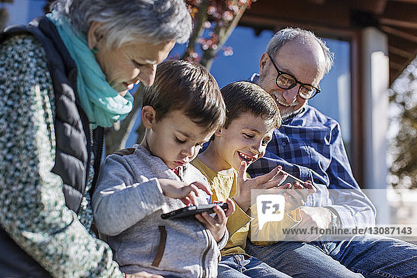 Glückliche Großeltern und Enkel benutzen Smartphones im Park