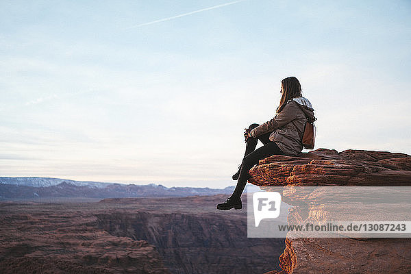 Seitenansicht einer auf einem Felsen sitzenden Frau bei der Hufeisenbeuge gegen den Himmel