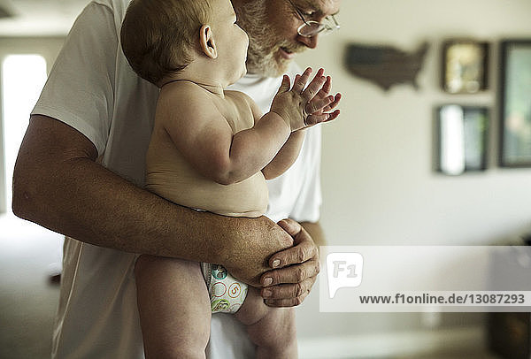 Grossvater trägt den hemdlosen Enkel  während er zu Hause steht