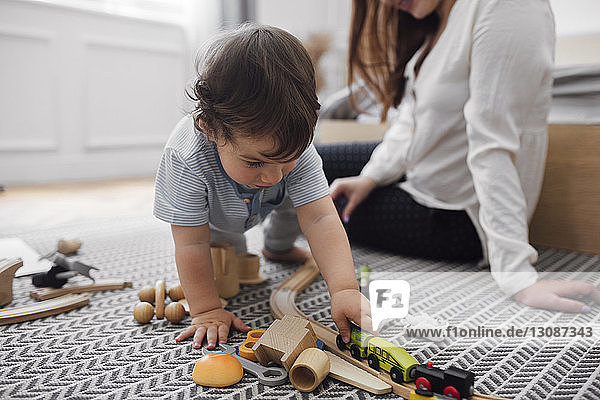 Kleiner Junge spielt zu Hause mit Miniatur-Eisenbahn der Mutter auf dem Teppich