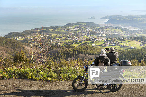 Älteres Ehepaar fotografiert Berge  während es mit dem Motorrad auf der Straße steht