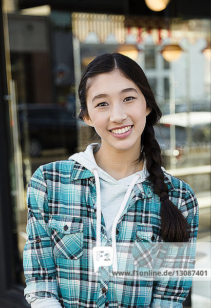 Portrait of smiling confident teenage girl with braided hair wearing plaid shirt in market