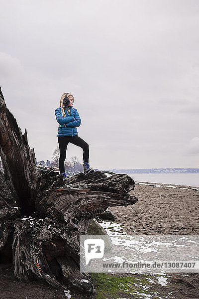 Girl standing on driftwood by lake against cloudy sky