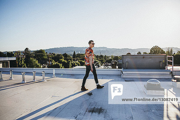 Modischer Mann in voller Länge geht auf Gebäudeterrasse bei klarem Himmel am sonnigen Tag