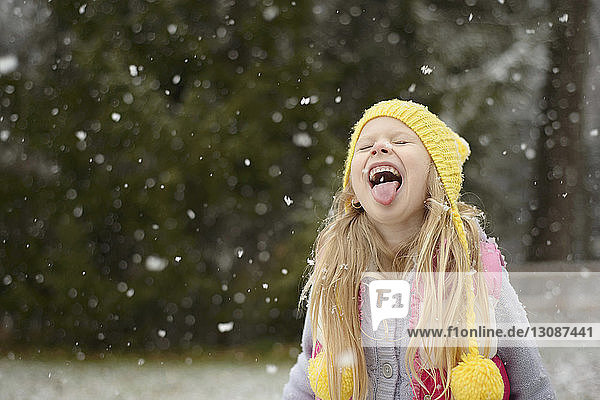 Verspieltes Mädchen streckt bei Schneefall die Zunge heraus
