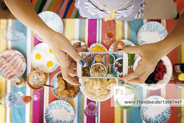 Ausgeschnittenes Bild von Frauenhänden beim Fotografieren von Essen bei Tisch