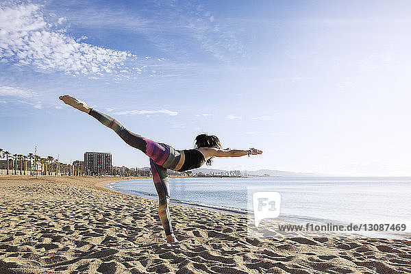 Entschlossene Frau  die am Strand Yoga in der Warrior 3-Pose macht