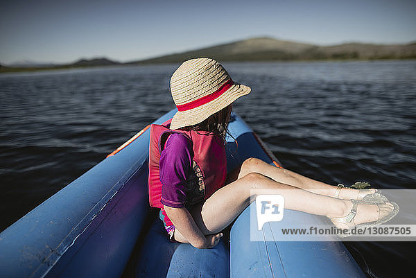 Seitenansicht eines nachdenklichen Mädchens mit Hut  das in einem aufblasbaren Floß auf dem See sitzt