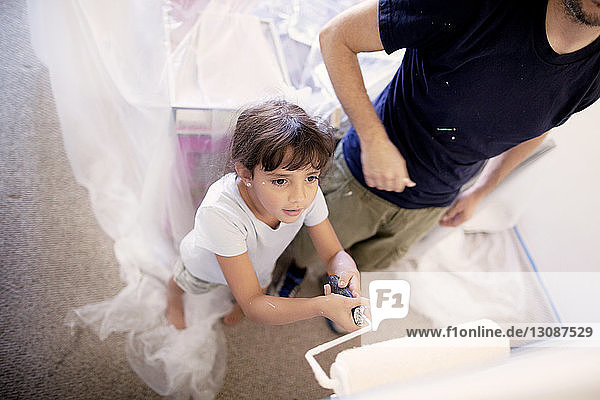 Girl standing besides father while painting wall at home