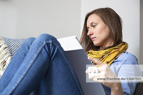 Frau liest Zeitschrift  während sie zu Hause auf dem Sofa sitzt