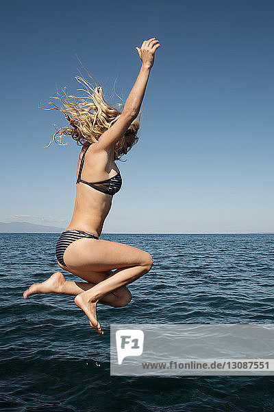 Sinnliche Frau im Bikini taucht im Meer vor klarem blauen Himmel