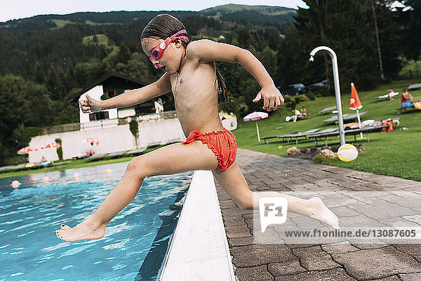Side view of shirtless girl jumping into swimming pool against mountain