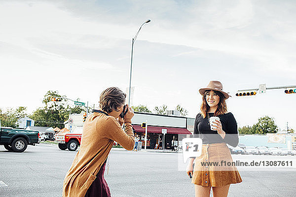 Frau fotografiert Freundin  während sie auf der Straße in der Stadt gegen den Himmel steht
