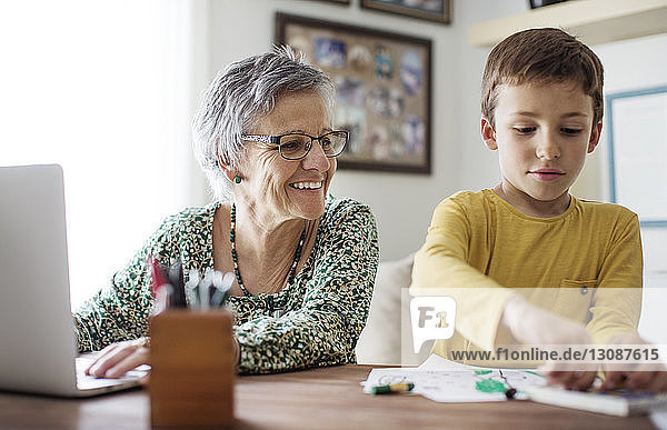 Glückliche ältere Frau schaut auf ihren Enkel  der zu Hause Buntstifte auswählt