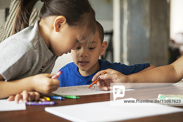 Children looking at mother drawing on paper while sitting in living room