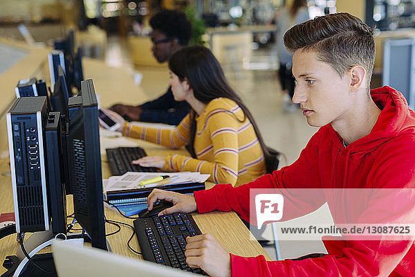 Freunde nutzen Desktop-Computer  während sie in der Bibliothek am Tisch sitzen