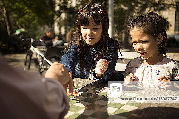 Schwestern spielen mit Großvater Dame  während sie im Park am Tisch sitzen