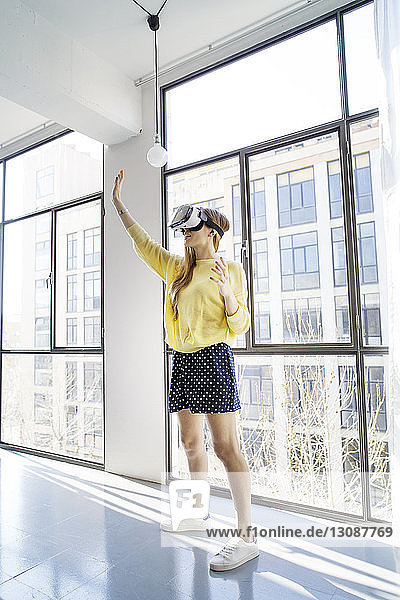 Businesswoman using virtual reality simulator while standing by window in office