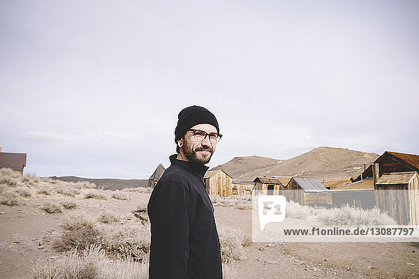 Porträt eines Mannes  der bei Blockhütten und Bergen gegen den Himmel in der Wüste steht