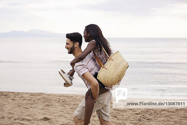 Seitenansicht eines Mannes  der eine Frau am Strand huckepack nimmt