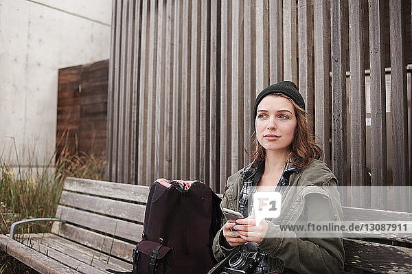 Nachdenkliche Wanderin hält Smartphone in der Hand  während sie auf Bank sitzt