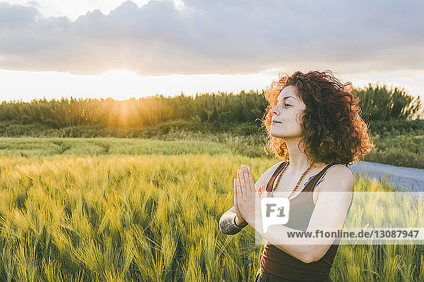 Frau meditiert  während sie bei Sonnenuntergang auf dem Bauernhof vor bewölktem Himmel steht