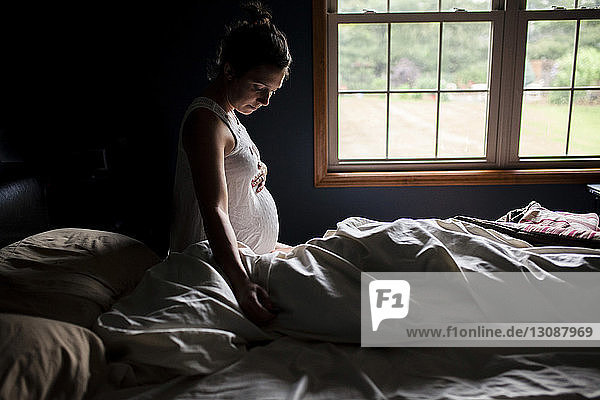 Side view of pregnant woman touching belly on bed at home