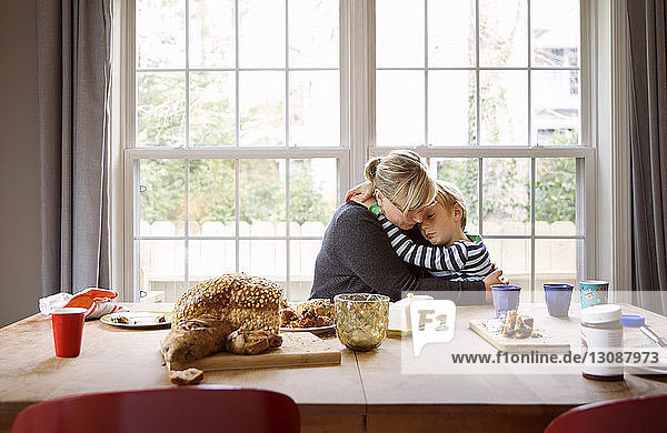 Liebende Mutter und Sohn beim Essen am Tisch gegen das Fenster im Wohnzimmer