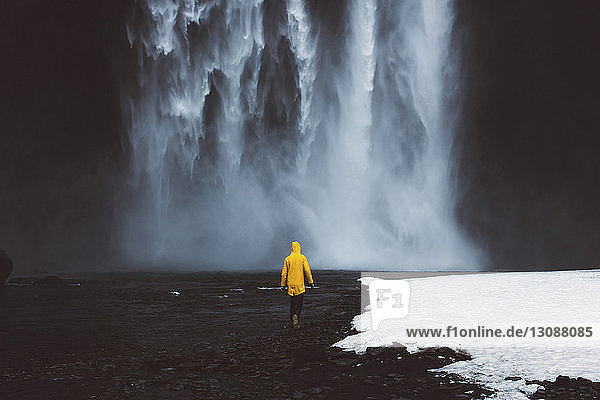 Rückansicht eines Mannes  der im Winter in Richtung Wasserfall geht