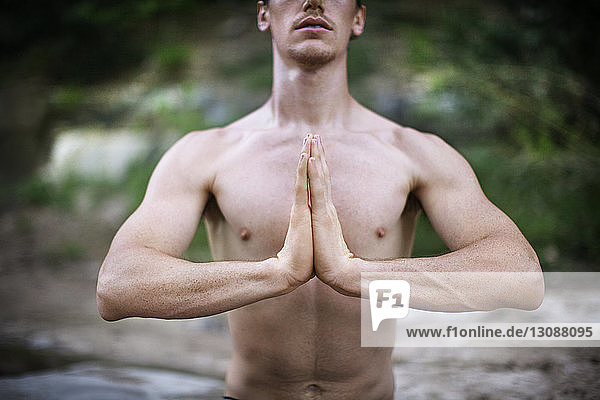 Mittellinie eines hemdlosen Mannes mit gefalteten Händen  der im Freien Yoga praktiziert