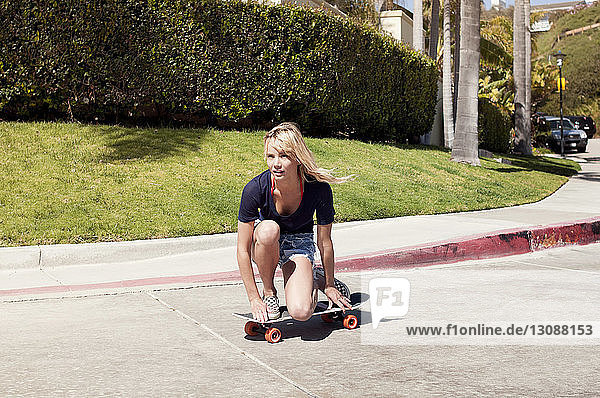 Nachdenkliche junge Frau kniend auf Skateboard auf der Strasse
