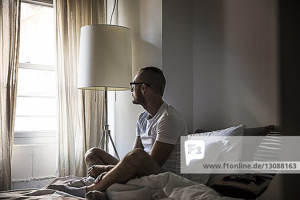 Thoughtful man looking away while sitting on bed at home