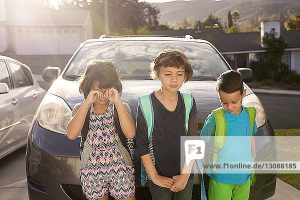 Upset siblings standing against car