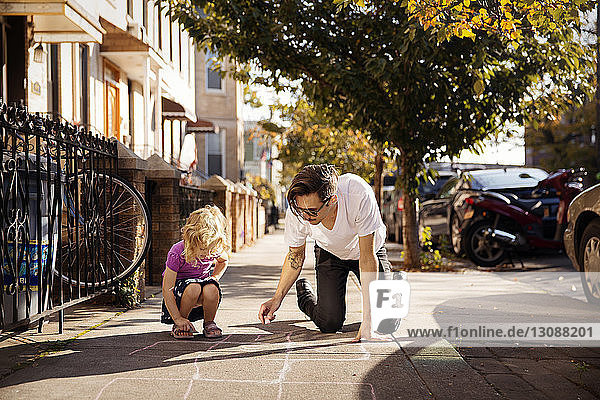 Tochter und Vater zeichnen Hüpfspiel auf Fußweg