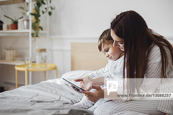 Mother and baby boy using tablet computer while sitting on bed