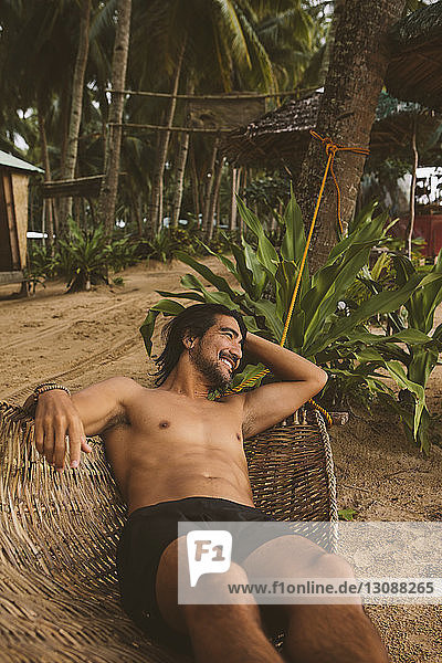 Hochwinkelansicht eines Mannes ohne Hemd  der beim Entspannen auf einer Hängematte am Strand wegschaut