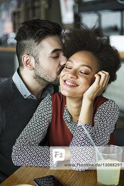Man kissing happy woman sitting in restaurant
