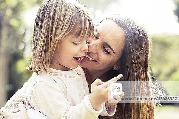 Glückliche Mutter mit Tochter benutzt Smartphone im Park