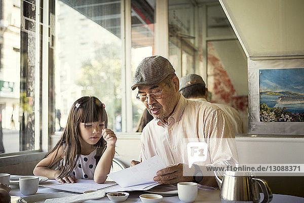 Grandfather showing paper to granddaughter while sitting in restaurant