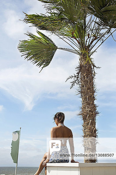 Rückansicht einer Frau  die auf einem Sitz am Strand gegen den Himmel sitzt