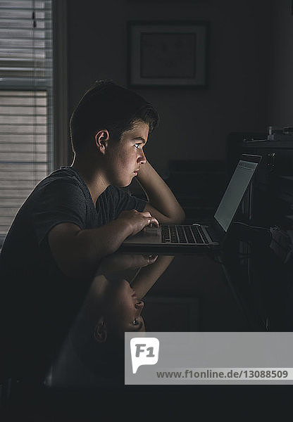 Seitenansicht eines ernsthaften Jungen  der einen Laptop-Computer in der Dunkelkammer benutzt