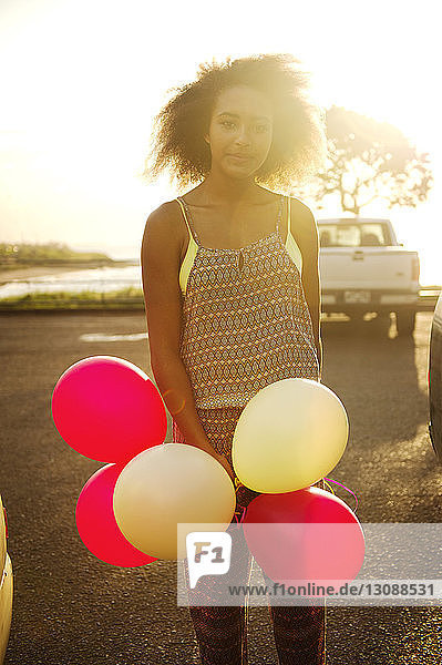 Portrait of teenage girl standing with balloons on field on sunny day