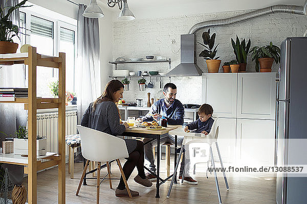 Eltern sehen ihren Sohn auf dem Hochstuhl sitzend beim Frühstück in der Küche