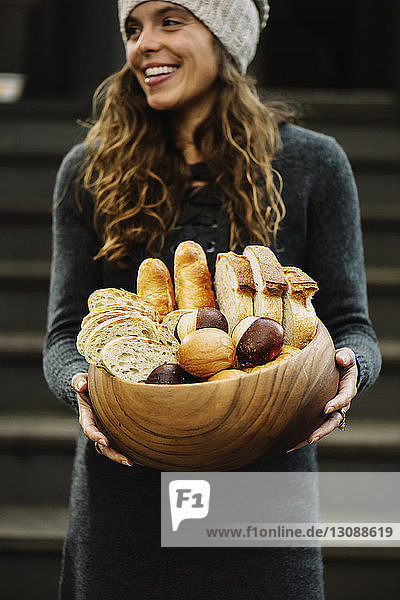 Glückliche Frau mit verschiedenen Brotsorten in Holzschüssel