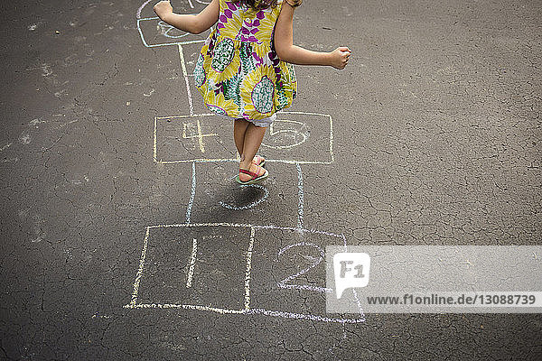 Low section of girl playing hopscotch on road
