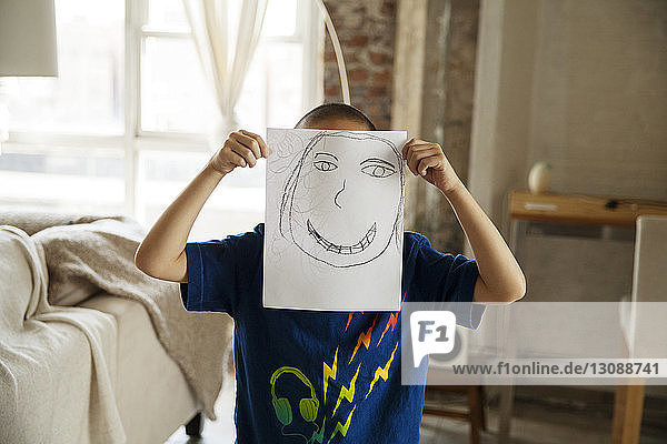 Junge zeigt Zeichnung  während er zu Hause im Wohnzimmer steht